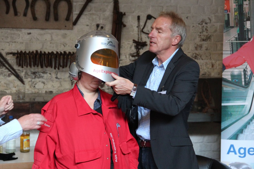 Lektorin Beate Kemper testet den Age Explorer. Heinz Einhaus, Mitarbeiter des Meyer-Hentschel Institut aus Saarbrücken, hilft ihr beim Anziehen.