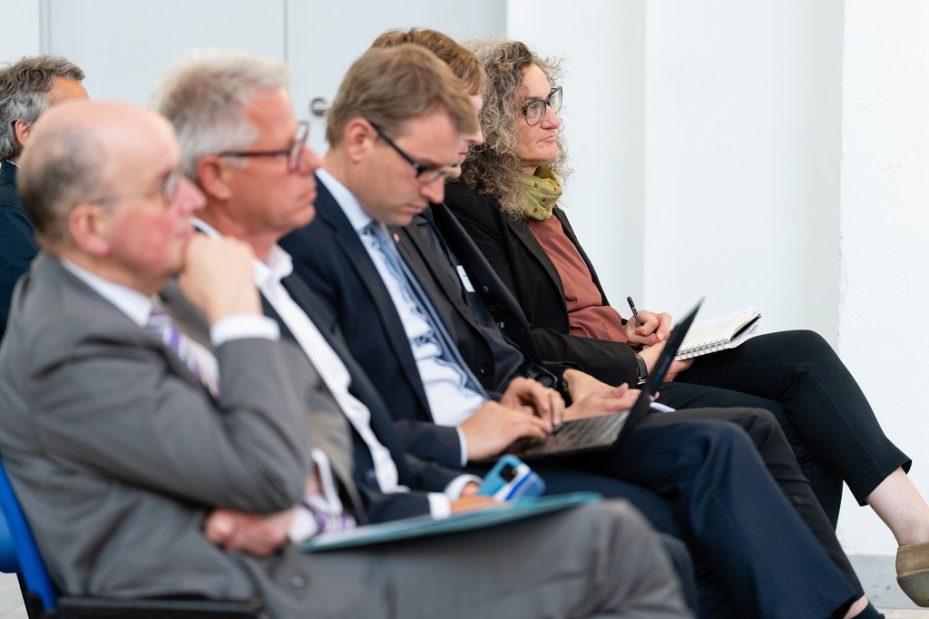 Mehrere Teilnehmer*innen der Konferenz sitzen auf ihren Plätzen und hören aufmerksam zu.